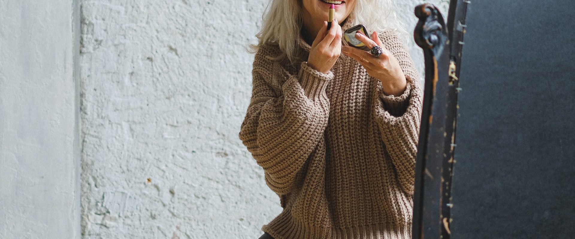 a mature woman applying makeup in the mirror